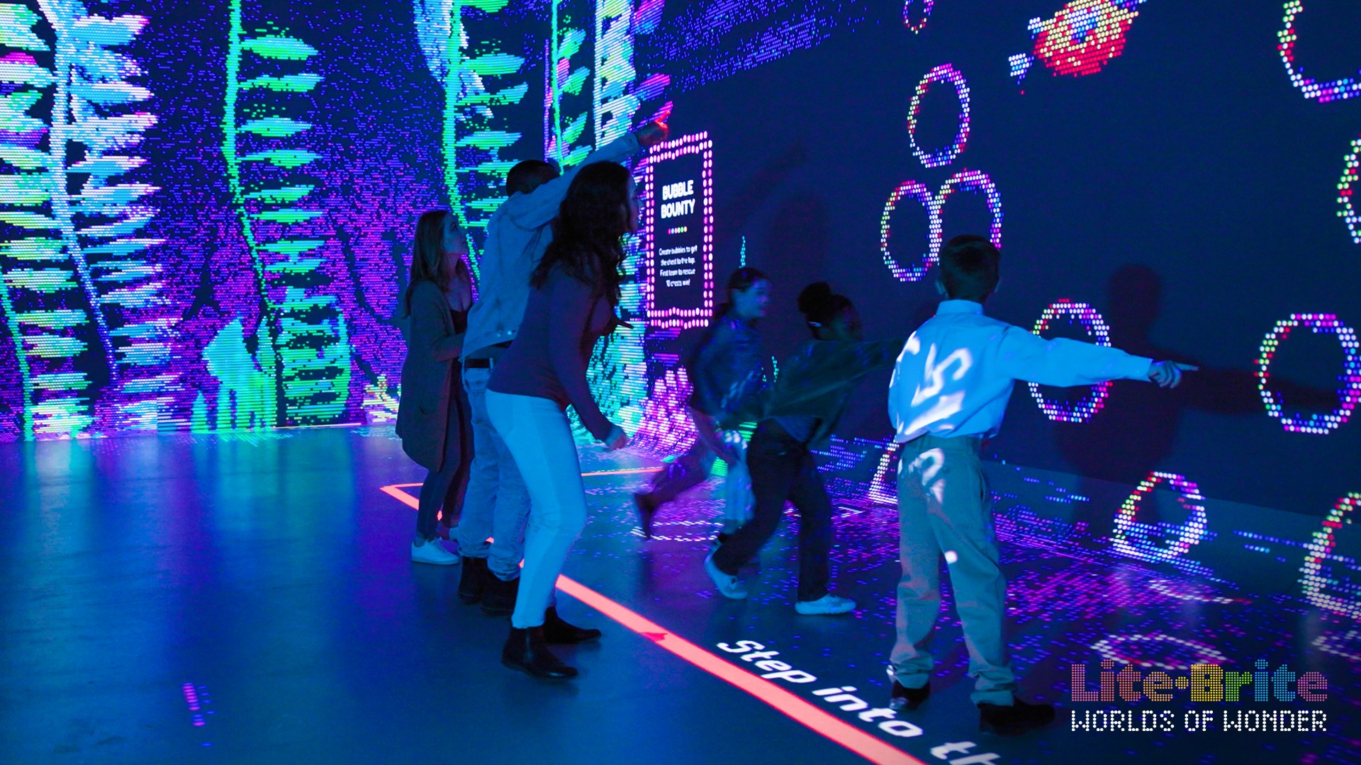 Guests reach for glowing bubbles on a Lite-Brite wall, with the Worlds of Wonder logo visible