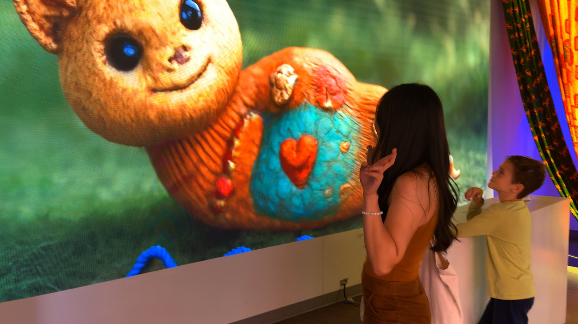 Guests stand beside a large colourful creature in the Mythos drawing experience