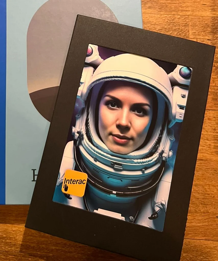 A printed astronaut portrait in a black presentation mount, with an Interac logo